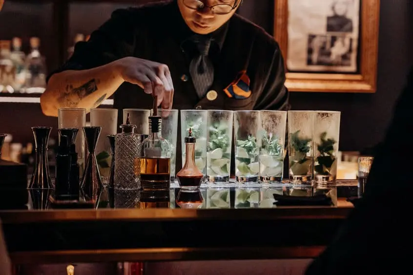 A bartender lining up highball glasses with mint at the bar