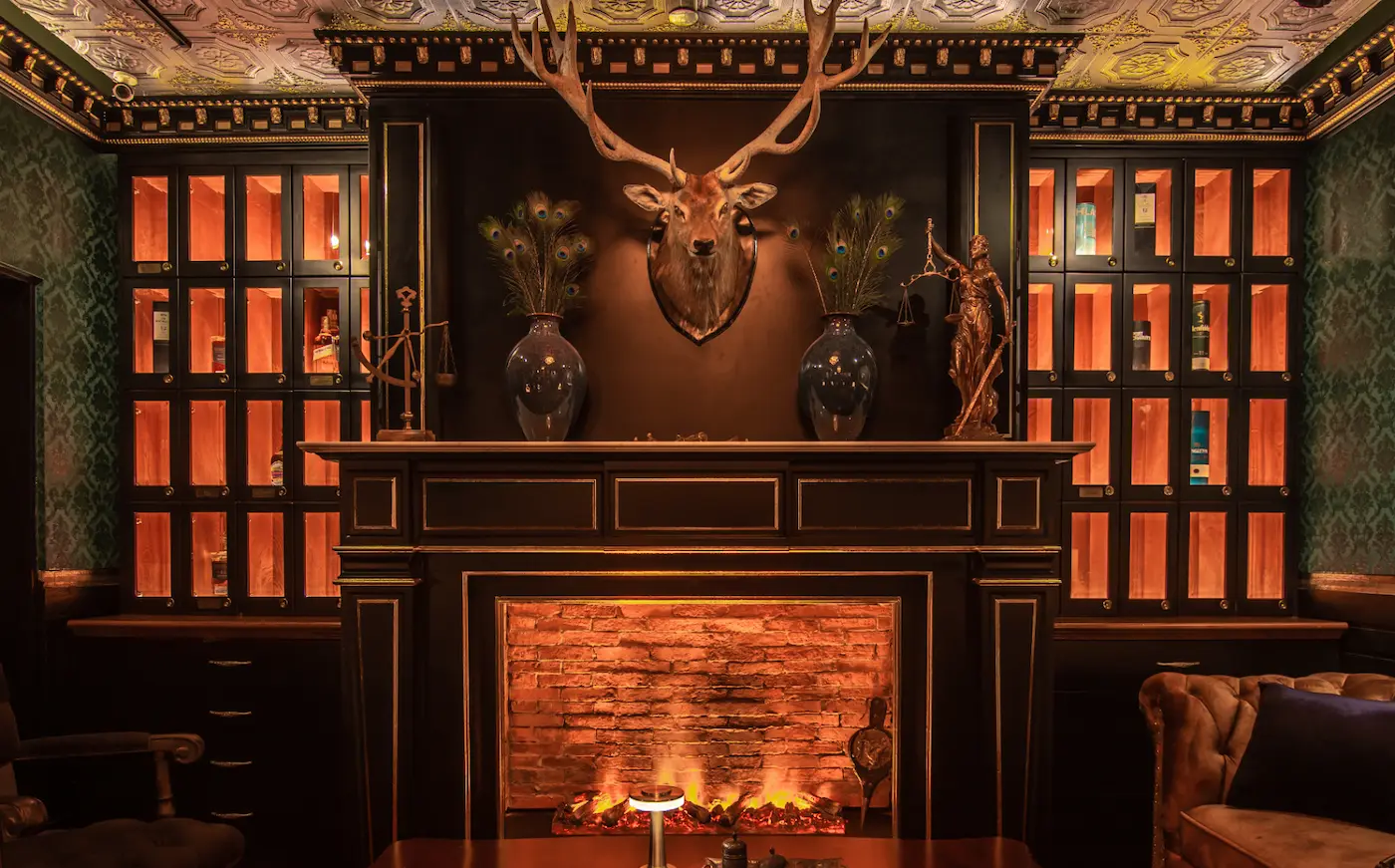 A wall of lit whisky lockers around the fireplace, with a mounted stag head above