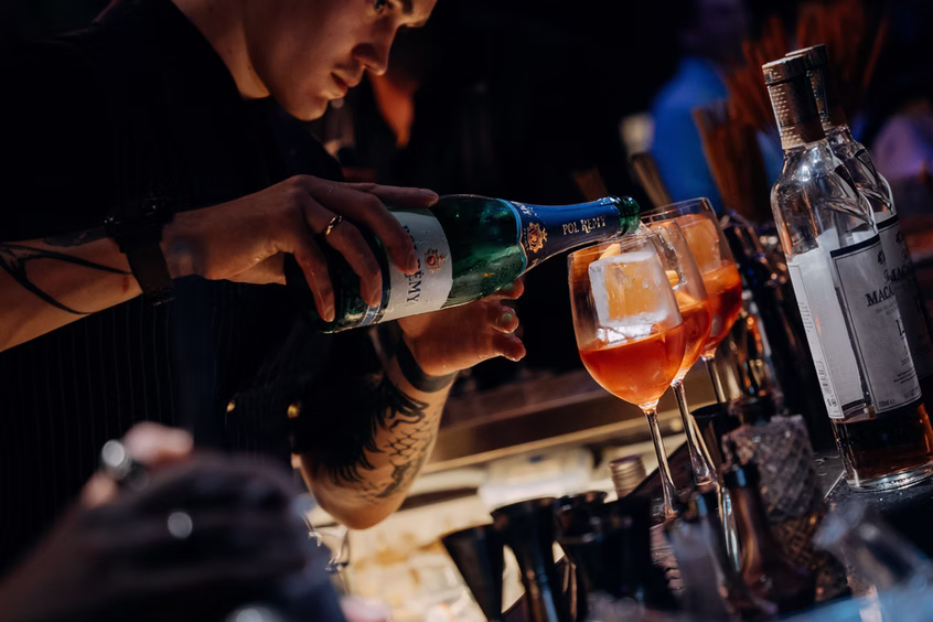 A bartender pouring sparkling wine into spritz glasses